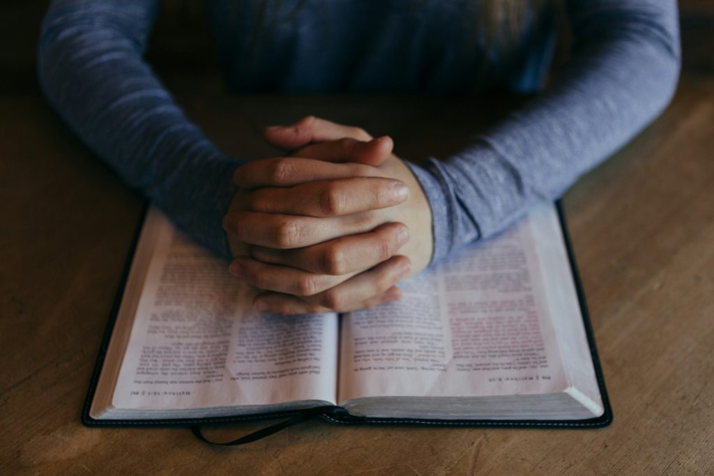 A man's hands folded on top of an open Bible